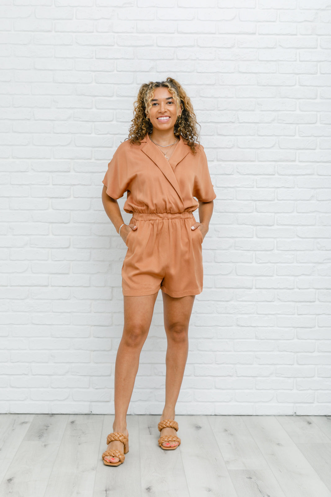 Camel-colored romper with a collared V-neckline, short sleeves, an elastic waistband, and functional pockets.