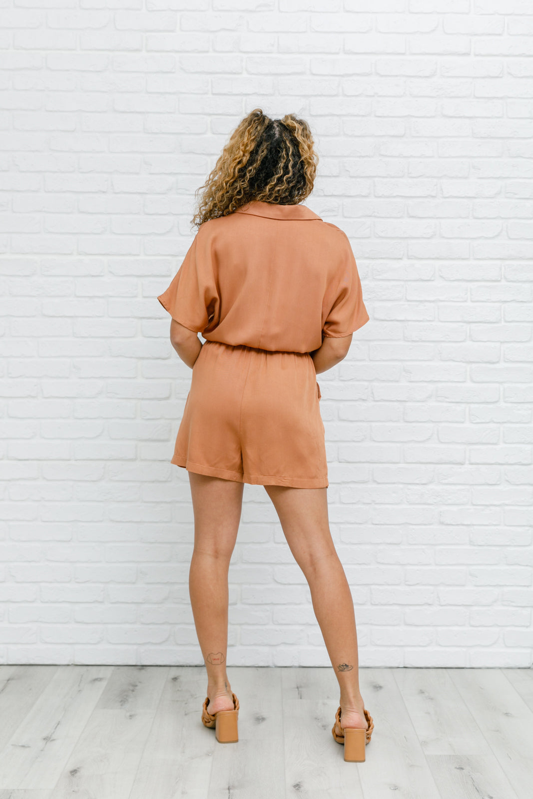 Camel-colored romper with a collared V-neckline, short sleeves, an elastic waistband, and functional pockets.