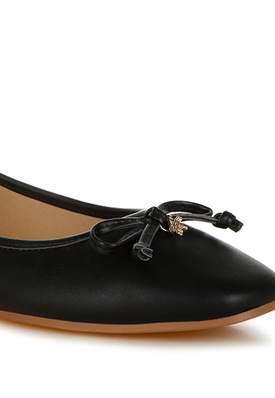 Close-up of black vegan leather ballerinas featuring delicate bow detail, smooth finish, and cushioned insole for all-day wear.