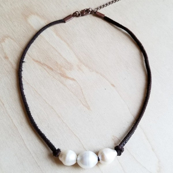 Flat lay of Maven Triple Freshwater Pearl Choker Necklace with three white pearls on a dark brown leather cord and adjustable closure.