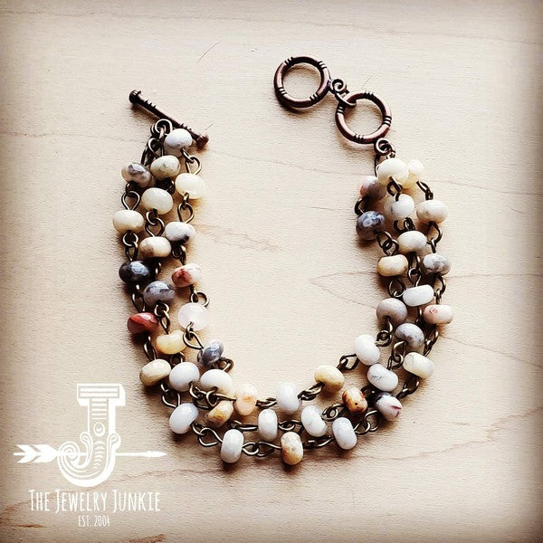 Curved view of handcrafted triple strand agate stone bracelet in earthy tones.