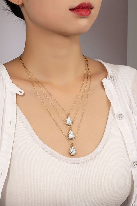 Woman wearing Torina Three Layer Teardrop Stone Pendant Necklace in white with layered chains and adjustable length.