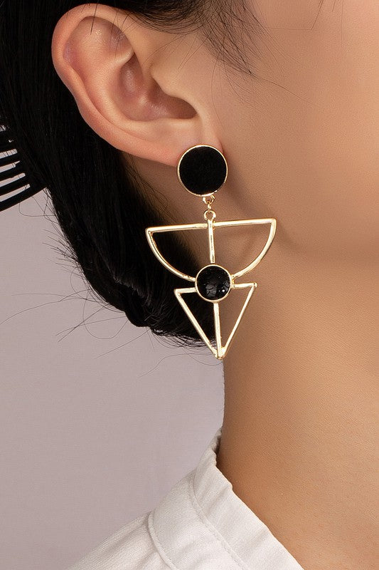 Gold earrings feature a velvet stud, geometric cutout design, and a textured black stone embedded in the cutout. They are 2.5 inches long.