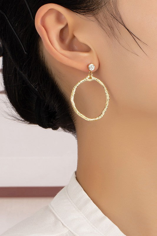 Woman wearing Hammered Hoop Drop Earrings with shiny gold hammered hoops and rhinestone studs, adding texture and sparkle.