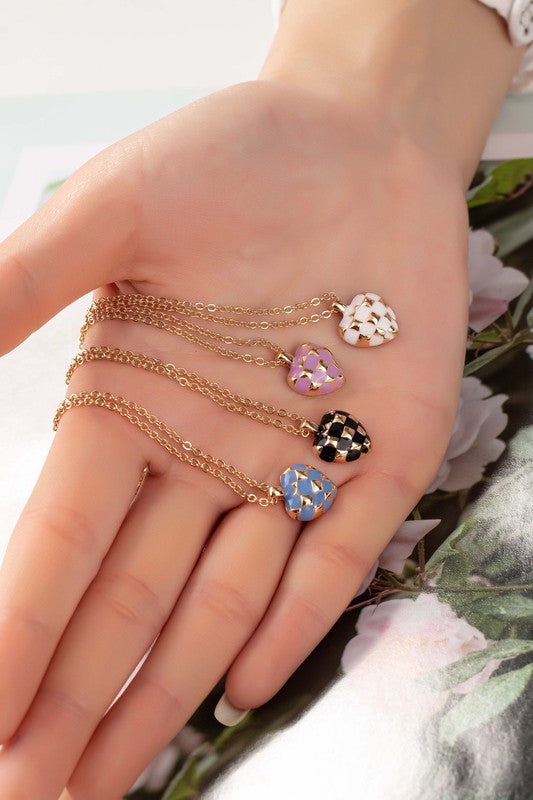 Woman’s hand holding four Mayley Checker Heart Pendant Necklaces in blue, black, pink, and white.