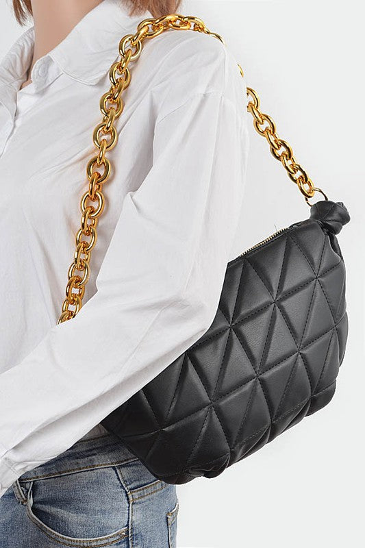 Woman holding black Mona Quilted Shoulder Bag over shoulder with chunky gold chain strap.