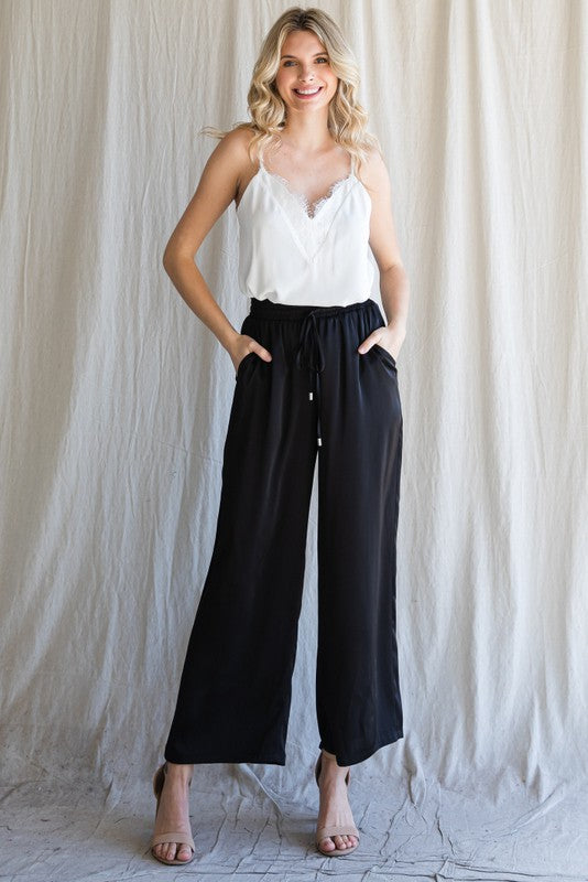 Model wearing Cita Wide Leg Bottoms in Black with high-waisted fit and flowy wide-leg silhouette.