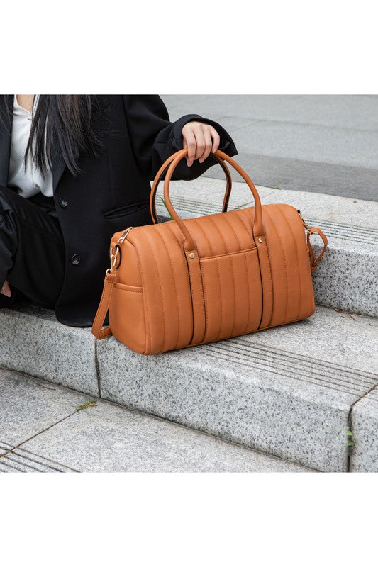 Luana Quilted Duffle Bag in Brown, woman seated holding bag by top handle.