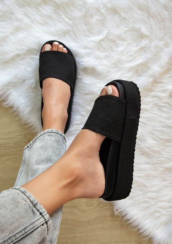 Woman wearing black Tina Woven Flatform Sandals with 2-inch cushioned sole, slip-on design, and woven strap detail.