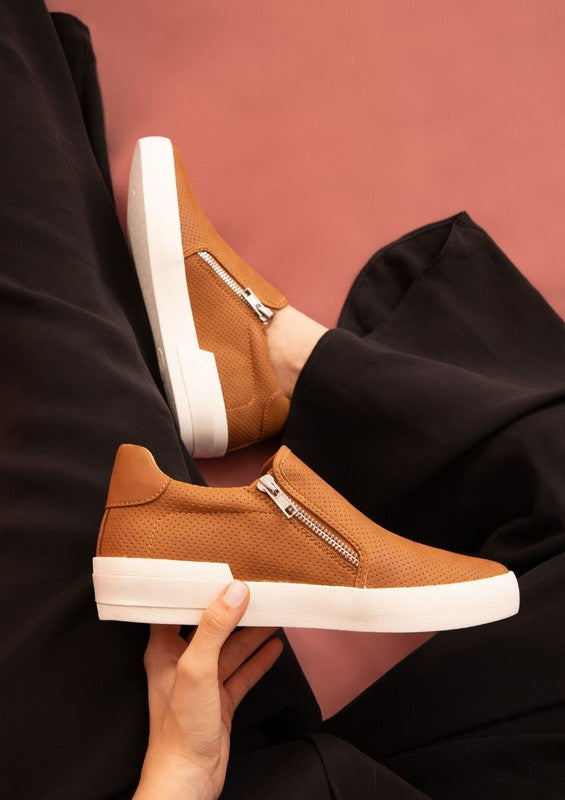 Tan slip-on sneakers with a round toe design and side zippers.