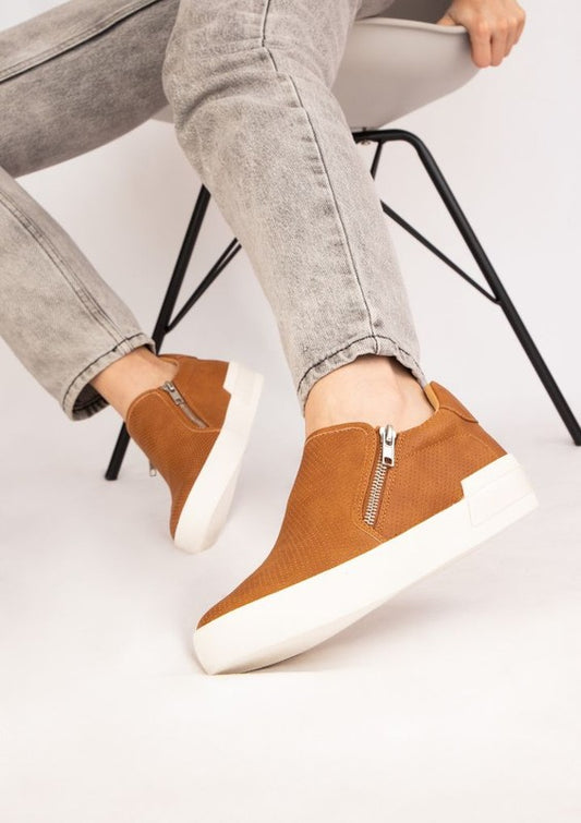 Tan slip-on sneakers with a round toe design and side zippers.