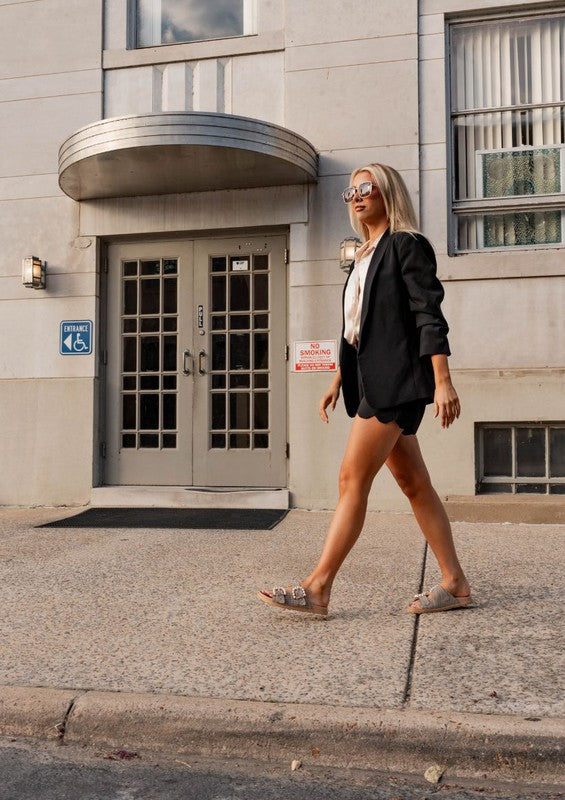 A stylish motion shot capturing a pretty woman walking in the Kelly Houndstooth Slides in nude, showcasing their casual elegance and comfortable fit in an everyday outfit.
