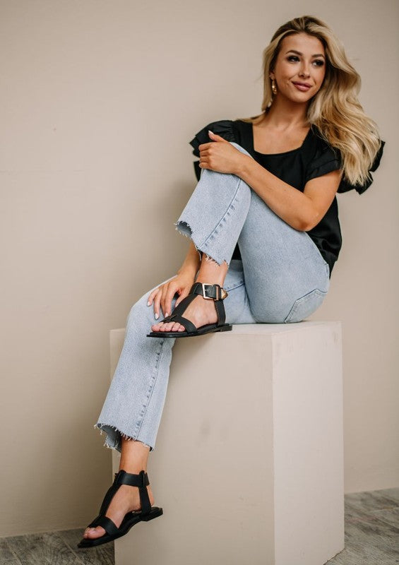 Woman wearing black leather wide strap sandals with ankle buckle closure.