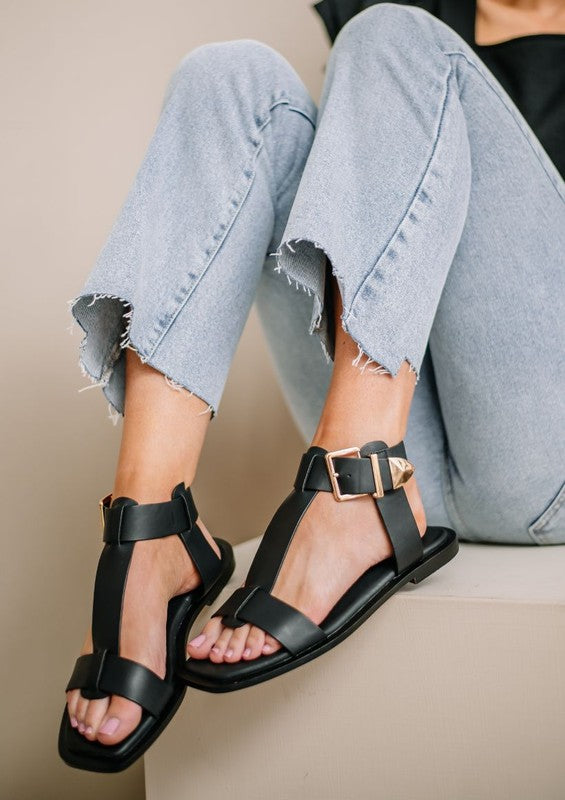 Woman wearing black wide strap flat sandals with oversized buckle hardware.
