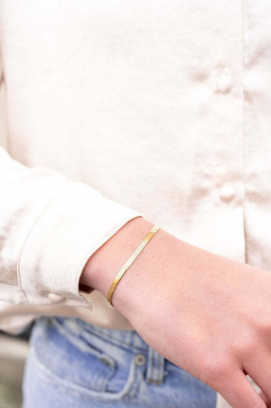 Woman wearing Kadence Gold Herringbone Bracelet on wrist, highlighting shiny gold finish and smooth herringbone pattern.