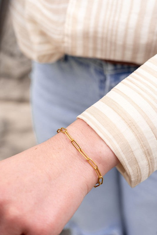 Woman wearing gold paper clip bracelet on wrist, highlighting adjustable fit and 18K gold-plated shine.