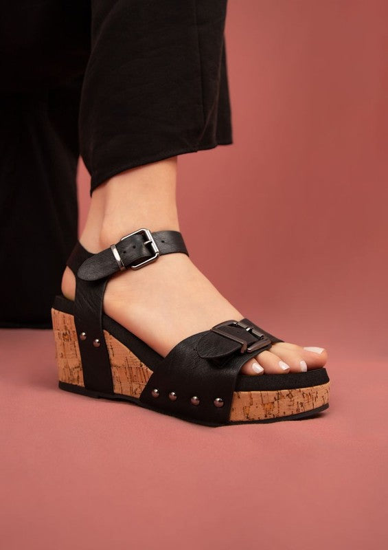 Black Romy Platform Sandals with oversized buckles, rivet accents, and vegan leather wedge design.