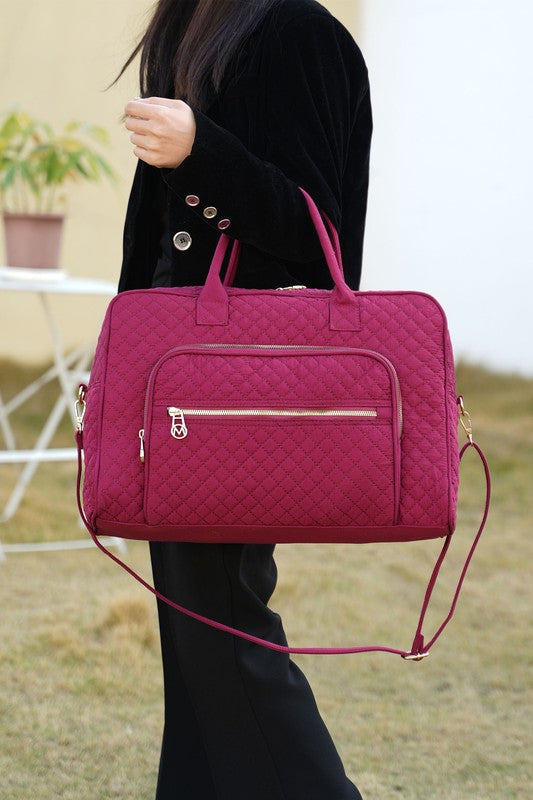 Woman holding fuchsia Jayla Quilted Duffle Bag by MKF, showing quilted texture and gold-tone accents.
