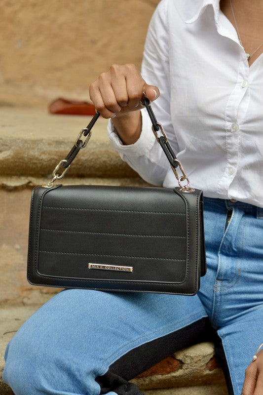 Woman holding olive MKF Dora Crossbody Bag by handle, showing silver-tone hardware.