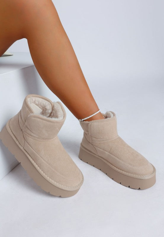 Woman wearing one Sand Holias Chunky Heeled Snow Boot with the matching boot displayed next to her.