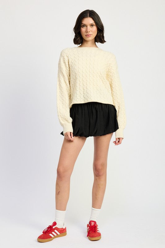Full body view of model in Kuuma Cable Knit Cropped Sweater, hands on hips, casual stance.