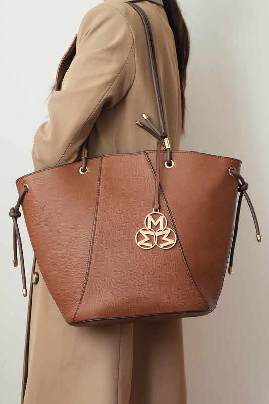 Woman wearing MKF Liv Tote Bag in brown over shoulder with gold-tone hardware.