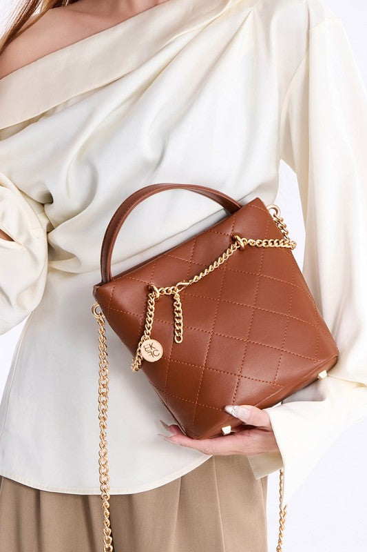 Woman holding brown MKF Damaris Crossbody Bag with quilted design and gold hardware.