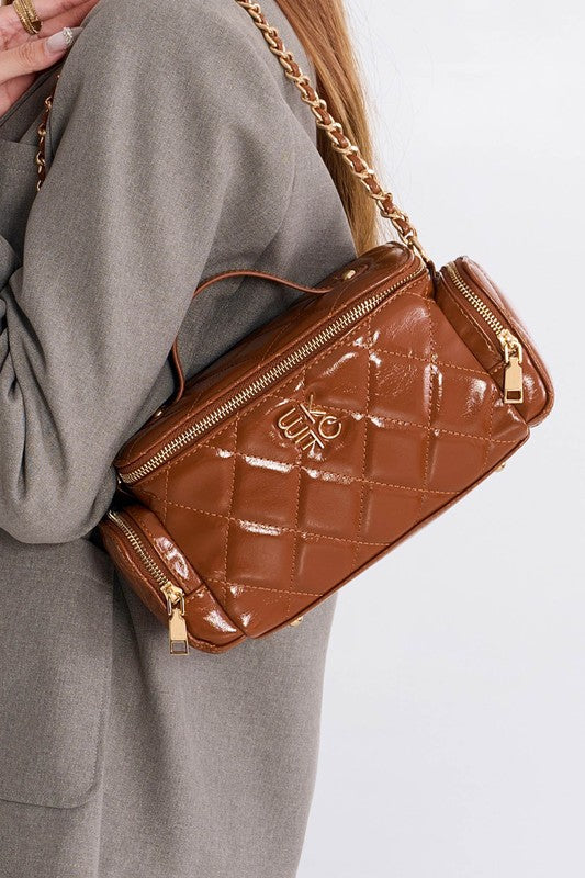 Woman wearing brown MKF Fortuna quilted crossbody purse with gold-tone chain strap over shoulder.