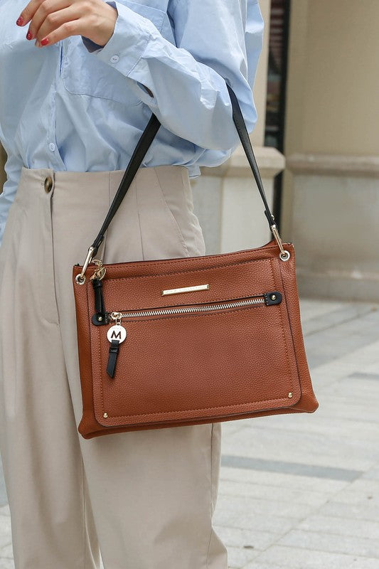 Woman holding cognac/black Aliyah shoulder bag by top handle with gold rings.
