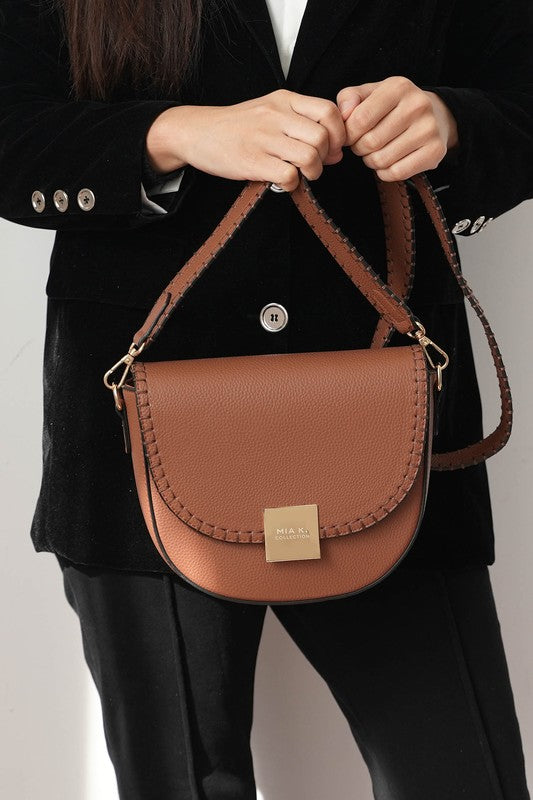 Woman holding cognac Isa crossbody bag by strap, gold-tone hardware visible..