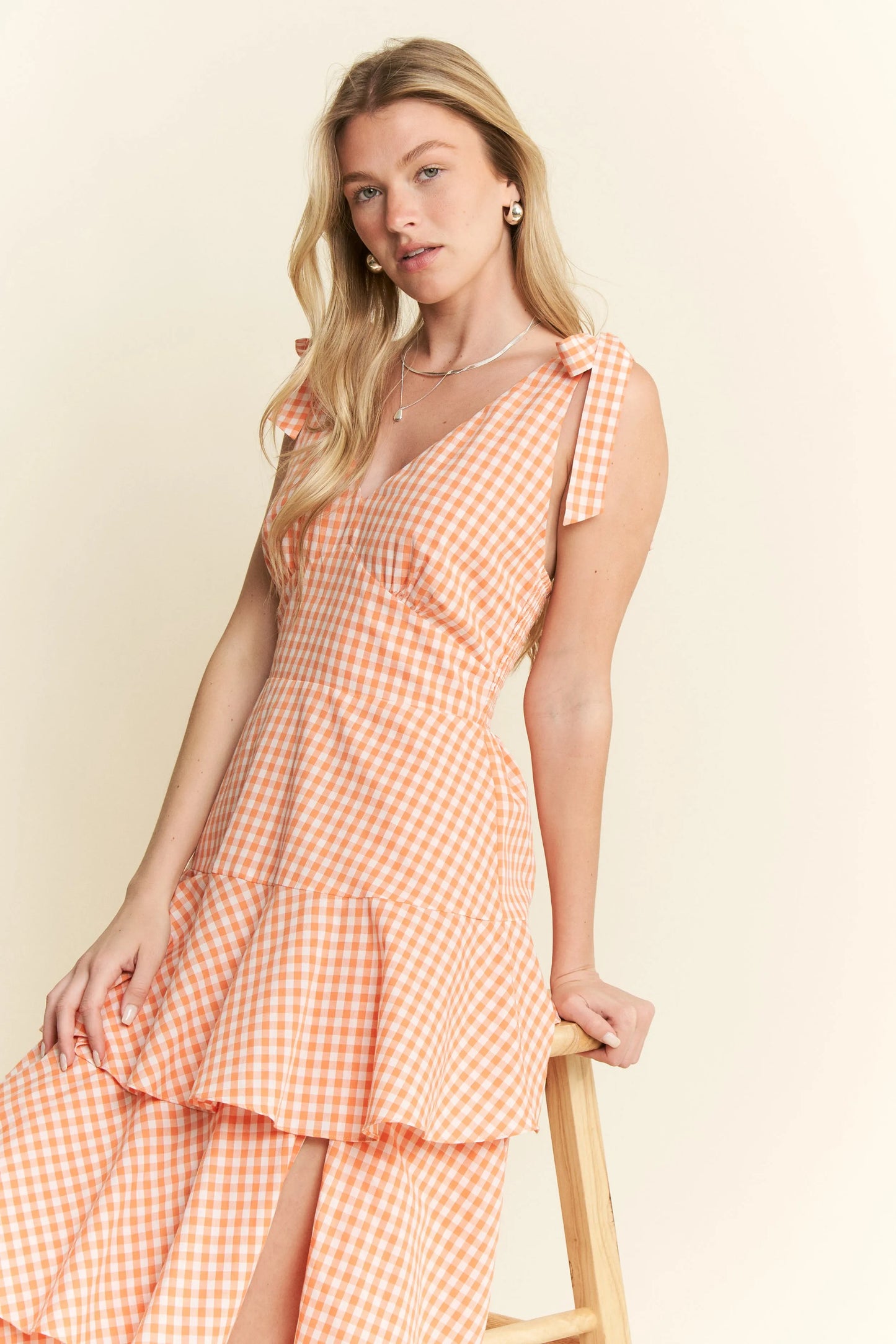 Close-up side view of model seated in Alice Gingham Tiered Midi Dress, highlighting halter ties, ruched back, and lightweight gingham fabric for a breezy summer vibe.