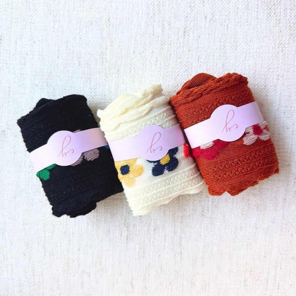 Rolled Side Garden Flower Socks in camel, white, and black placed next to each other.