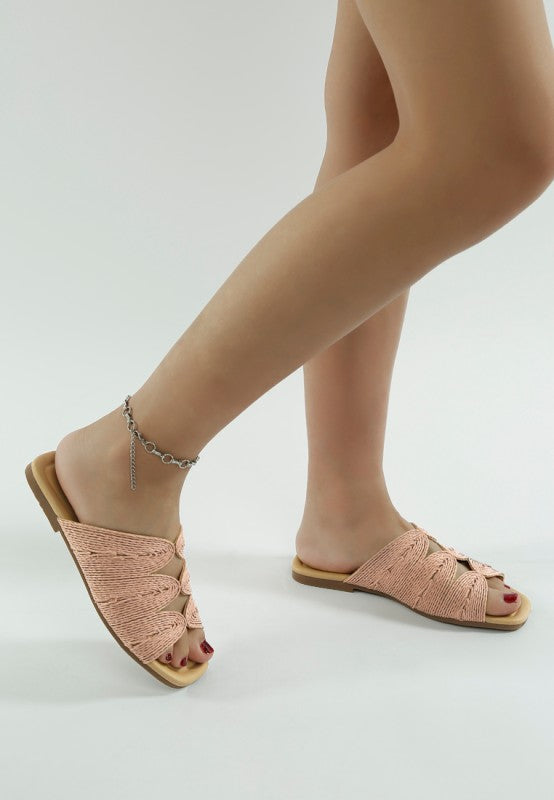 Side view of woman wearing dusty pink Daisy Doe raffia flats, highlighting the slip-on design and flat heel.