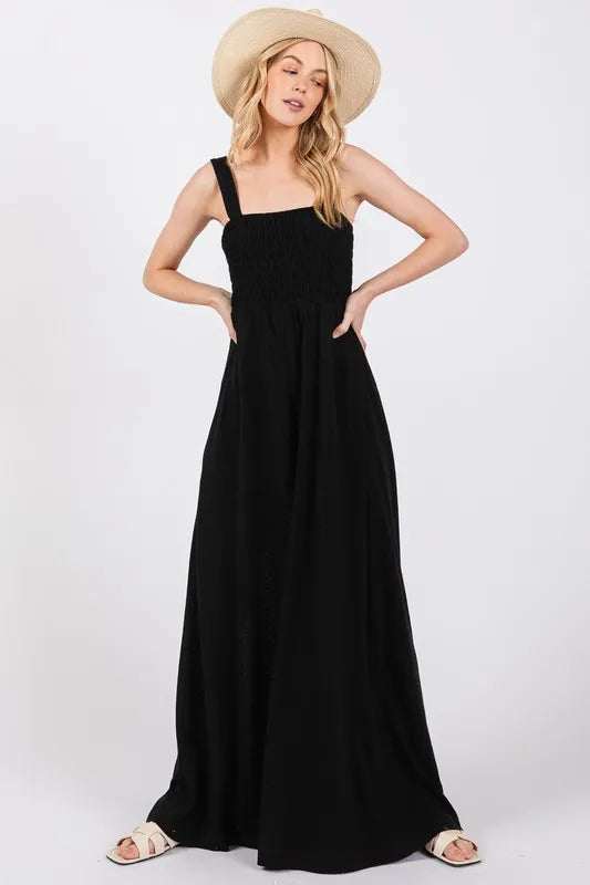 Fashionable black jumpsuit featuring a stretchy smocked bodice and flowy wide legs, made from a breathable cotton-polyester blend.