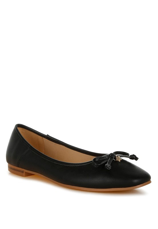 Black faux leather ballerinas with a bow embellishment, round closed toe, cushioned insoles, and flat heel. Slip-on design for easy wear.