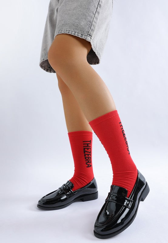 Side view of model wearing Black Avery Patent Loafers styled with socks and shorts, showing flat heel design.