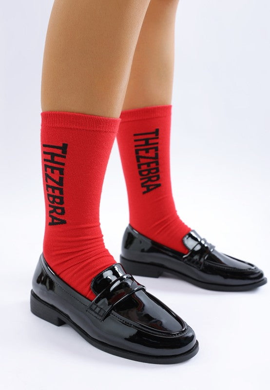Side view of Black Avery Patent Loafers highlighting glossy patent finish, penny strap detail, and flat heel design.