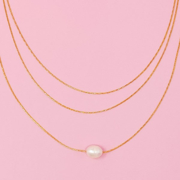Flat lay of layered freshwater pearl pendant necklace on pink background