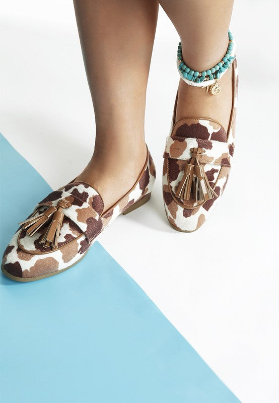 Model wearing both Moraug cowprint loafers with tassel accents, highlighting the playful print, faux suede material, and low block heel by Rag Company