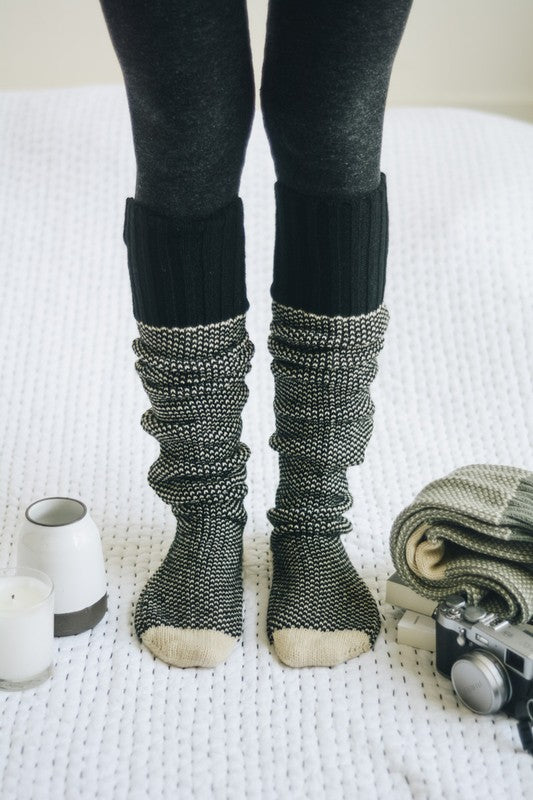 Woman standing in black Jerica Lounge Socks, knee-high oversized knit style.