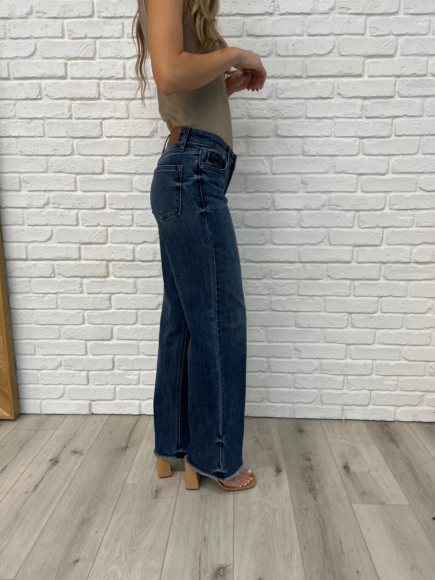Side view of the Addie Mid Rise Wide Leg Jeans by Judy Blue in dark vintage wash, featuring raw cut-off hem, release hem dye detail, and a 93% cotton blend for a retro-inspired look with modern flair.