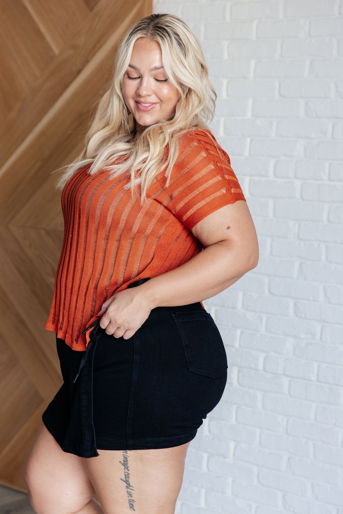 Side view of a plus size model wearing the Aaliyah Loose Knit Top in burnt orange with a wide v-neckline, short sleeves, and a lightweight open knit stripe pattern.