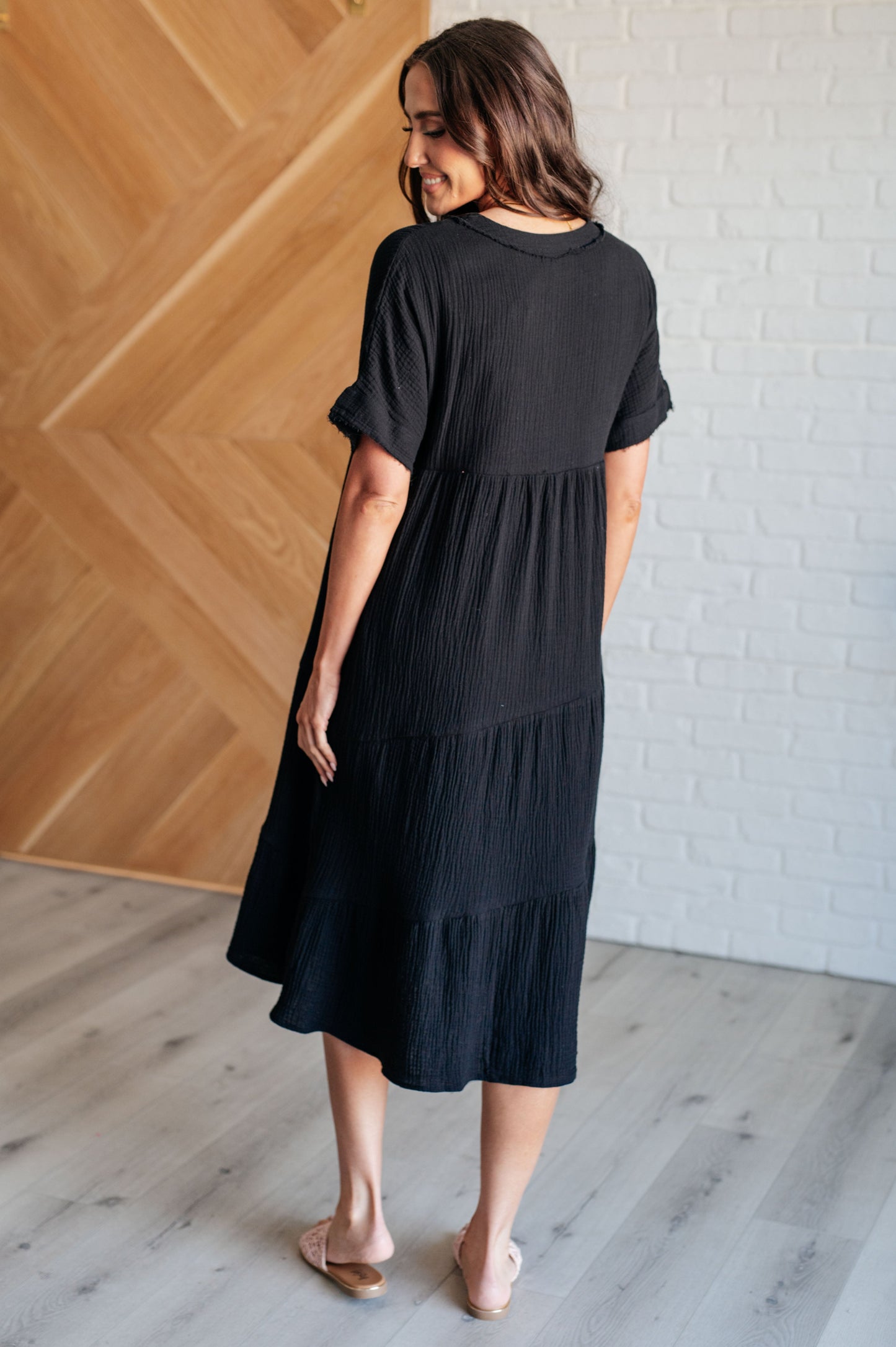 Back view of black Dani Dolman Sleeve Dress with raw edge details, pockets, and relaxed tiered midi cut.