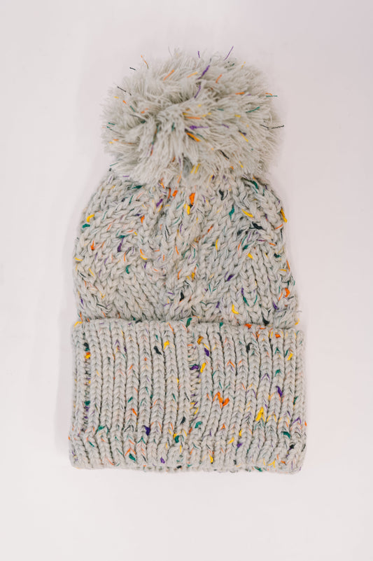 Front view of Cover Your Ears Pom Pom Beanie showing cable knit and speckled texture.