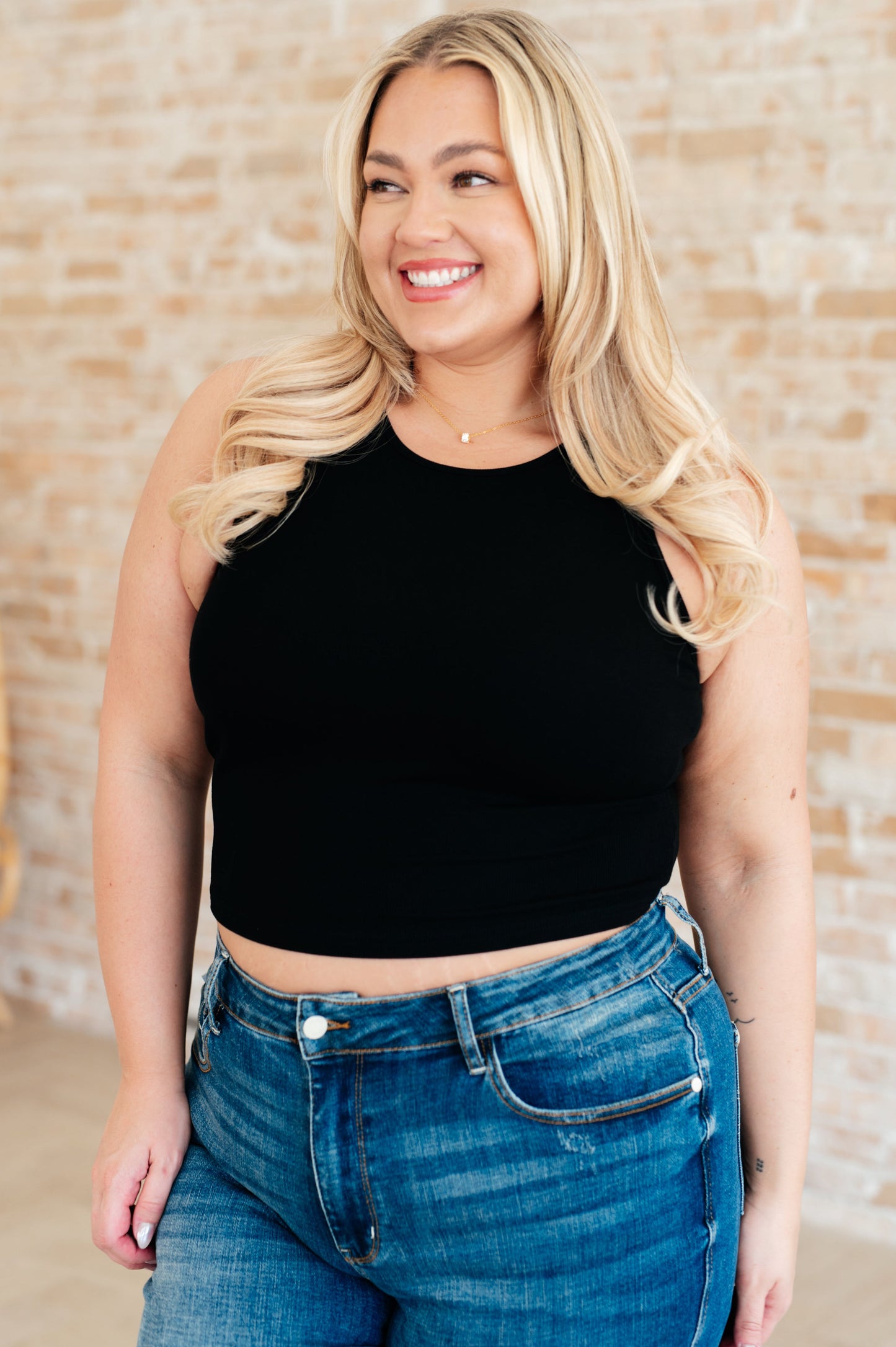 Plus size model in black ribbed crop tank top front view, sleeveless round neckline, trendy summer layering top.