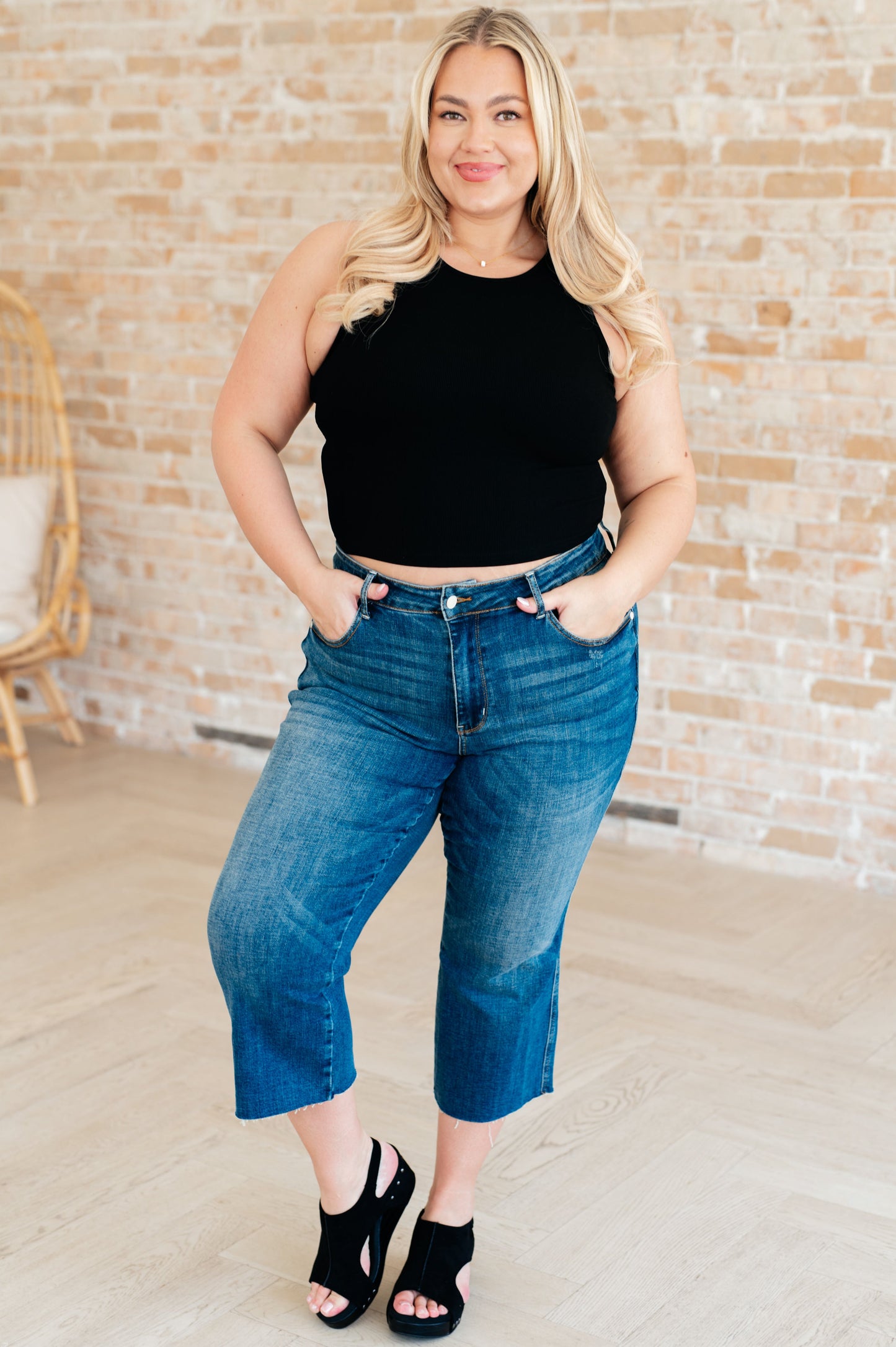 Plus size model wearing black rib knit crop tank styled with jeans, sleeveless round neckline, breezy summer look.