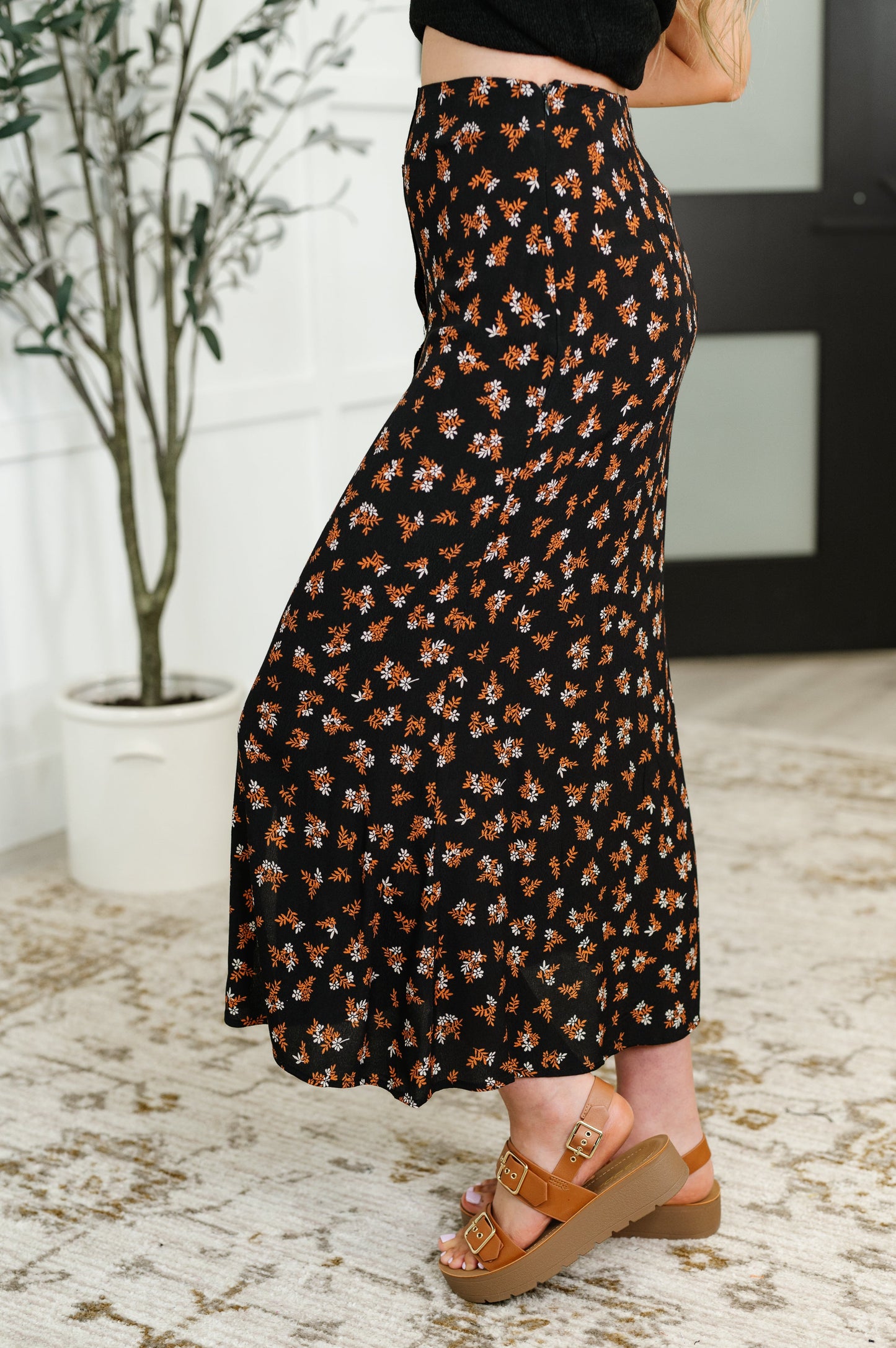 Side view of the Luisa Midi Skirt in black, showcasing the floral pattern, high-waisted fit, and subtle front slit detail.
