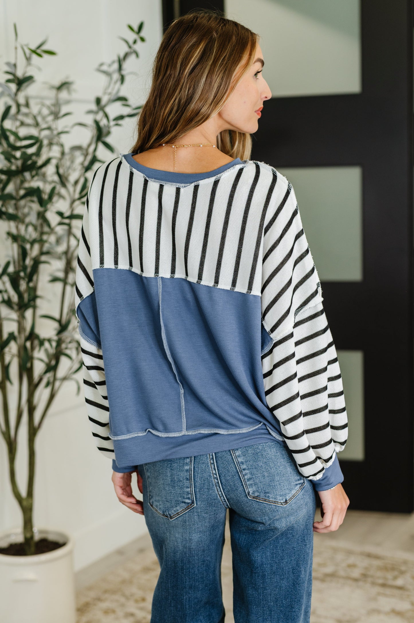 Back view striped crew neck pullover with exposed seam and denim detail.