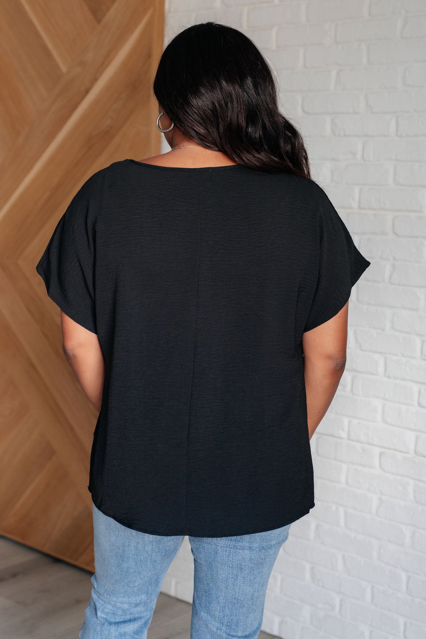 Plus-size model back view of Freya black V-neck top with relaxed silhouette and woven texture.