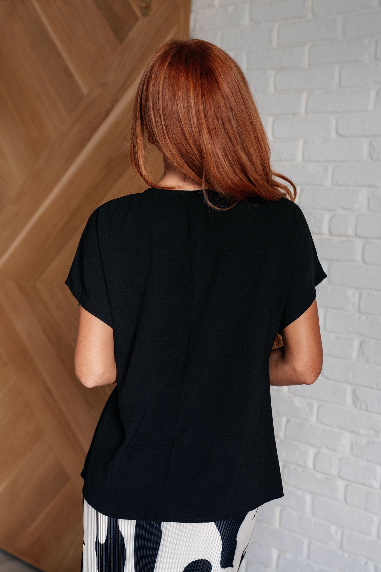 Back view of Freya black V-neck top with seam detail and flowy drape.